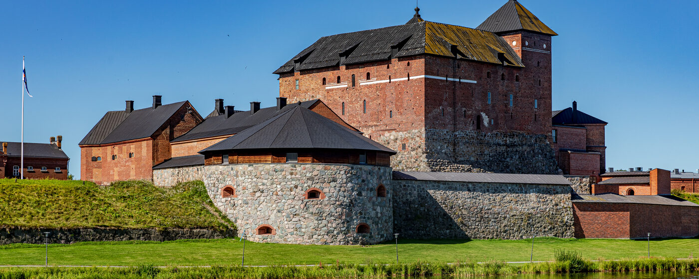 Hämeen linna punatiilisine muureineen ja torneineen Vanajaveden rannalla kirkkaana kesäpäivänä.